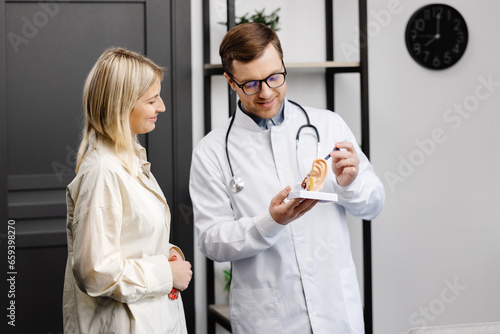 A young attractive otolaryngologist doctor shows a model of the ear and tells the patient about the structure of the ear