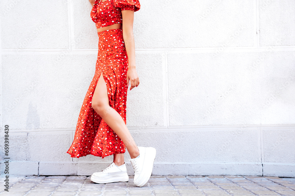 Young beautiful hipster woman in trendy summer red dress. Carefree woman posing in the street near wall. Model outdoors in at sunny day. Cheerful and happy. No face Young beautiful hipster woman in trendy summer red dress. Carefree woman posing in the street near wall. Model outdoors in at sunny day. Cheerful and happy. No face