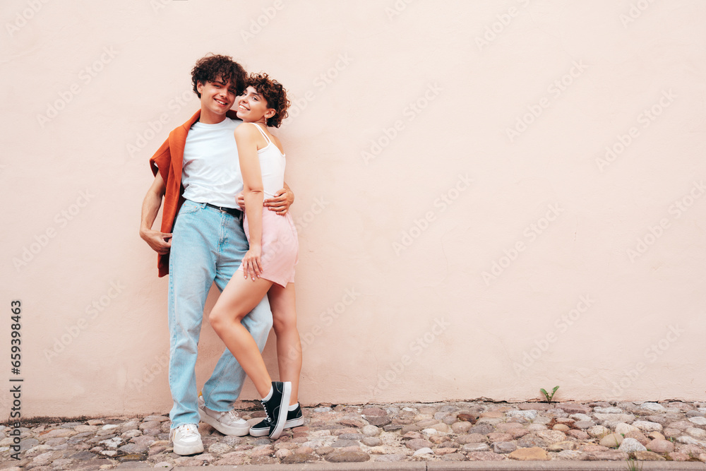 Young smiling beautiful woman and her handsome boyfriend in casual summer white t-shirt and jeans clothes. Happy cheerful family. Female having fun. Couple posing in the street near wall