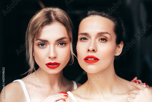 Closeup portrait of two young beautiful smiling brunette female with glamour evening makeup. Sexy women with healthy glowing face skin. Hot models with red lips posing over dark background