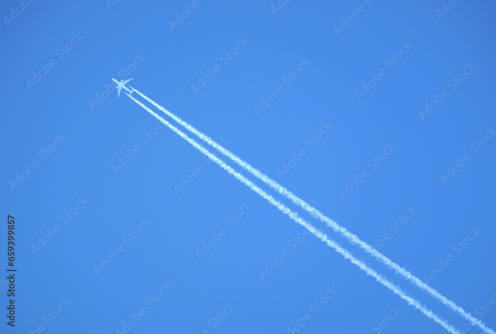 Large two engine passenger supersonic airplane flying from right to left high in blue cloudless sky leaving long white track Large two engine passenger supersonic airplane flying from right to left high in blue cloudless sky leaving long white track