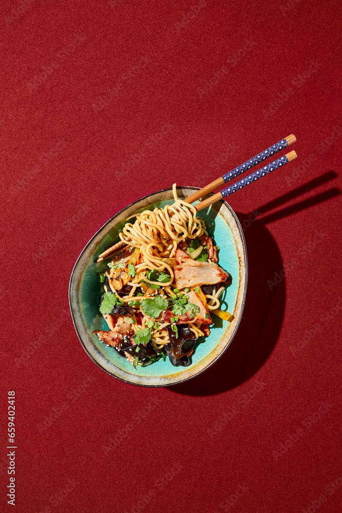 From a top perspective, Asian wheat noodles with chicken and muer mushrooms captivate in a ceramic bowl. Twisted around chopsticks. From a top perspective, Asian wheat noodles with chicken and muer mushrooms captivate in a ceramic bowl. Twisted around chopsticks.