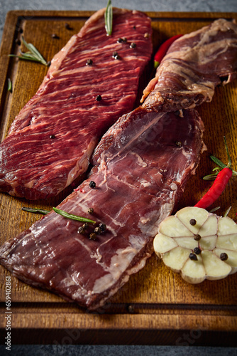 Close-up, vertical side view, underscoring the intricate marbling of the diaphragm steak. This alternative beef cut is elegantly placed on a wooden board with a gray tone
