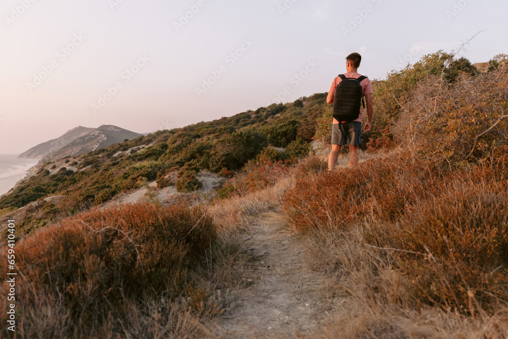 Hiker man in a T-shirt and shorts with backpack walking on the coast
