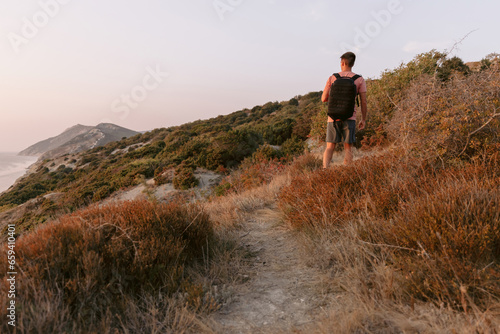 Hiker man in a T-shirt and shorts with backpack walking on the coast