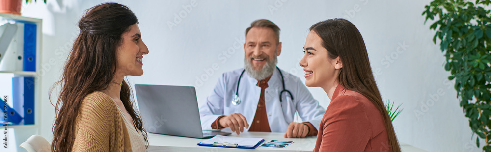 happy lesbian couple looking cheerfully at each other during doctor appointment, ivf concept, banner happy lesbian couple looking cheerfully at each other during doctor appointment, ivf concept, banner