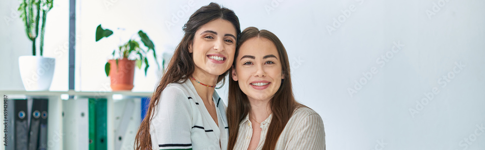 two joyful lesbians at doctor's office smiling at camera and hugging each other, ivf concept, banner two joyful lesbians at doctor's office smiling at camera and hugging each other, ivf concept, banner