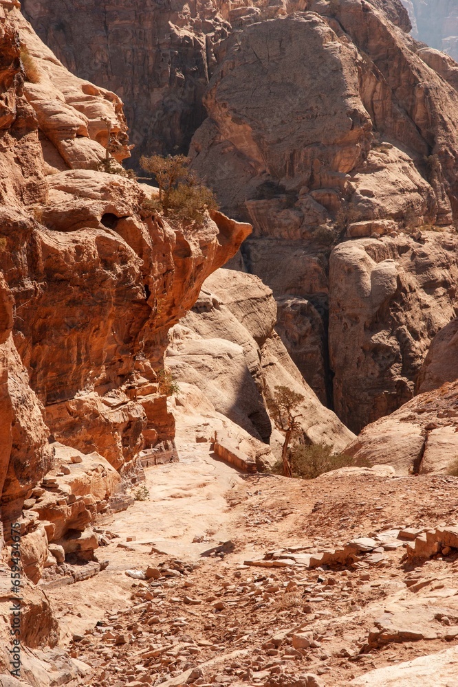 Jordan, Petra, Narrow road to Ad Deir monastery. Blurred background. Selective focus. Mountain landscapes with steep abysses. Road between rocks going up. Rocky rocks of red, pink and orange tones.