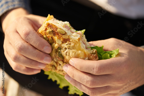 Men's hands hold a fresh sandwich, a clear and sunny day.