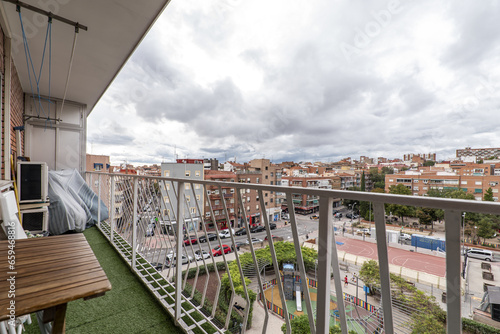 a terrace with artificial grass floor with white railing, clothesline on the ceiling, wooden table and folding chairs