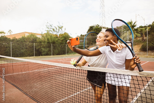 Portrait of two young beautiful women with tennis clothes and rackets in a tennis court ready to play a game. © Jordi Salas