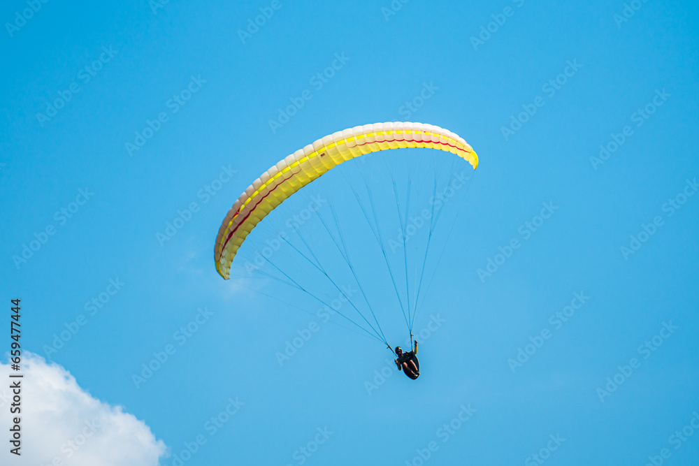 An adrenaline-pumping extreme sport, paragliding against the clear blue sky. Paraglider flying with his parachute above the sky with a background of blue sky and white clouds in a sunny day. An adrenaline-pumping extreme sport, paragliding against the clear blue sky. Paraglider flying with his parachute above the sky with a background of blue sky and white clouds in a sunny day.