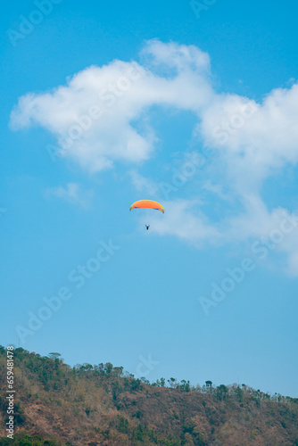 Paragliding attraction flying across hilly areas and clear blue skies. Paragliding is a sport that stimulates adrenaline by flying using a parachute in the wide sky