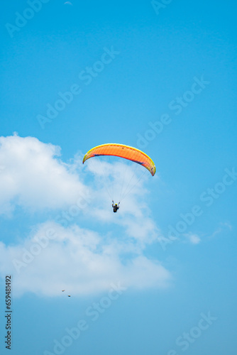 An adrenaline-pumping extreme sport, paragliding against the clear blue sky. Paraglider flying with his parachute above the sky with a background of blue sky and white clouds in a sunny day.