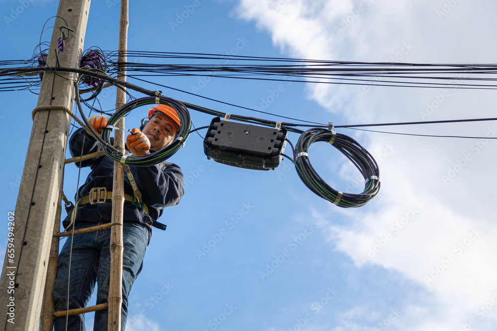 A technician working on ladder carefully for maintenance fiber optic wires attached to electric poles. Safety equipment and Operational safety. - obrazy, fototapety, plakaty 