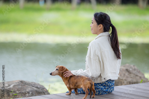 Woman sit with her dachshund dog at lake side in park