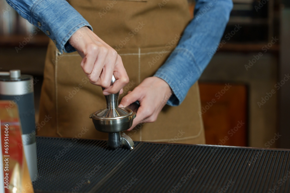 Young Asian business barista in a dark blue shirt wearing a brown apron. Grind coffee beans and brew coffee behind the coffee machine counter in a coffee shop. small family business Young Asian business barista in a dark blue shirt wearing a brown apron. Grind coffee beans and brew coffee behind the coffee machine counter in a coffee shop. small family business