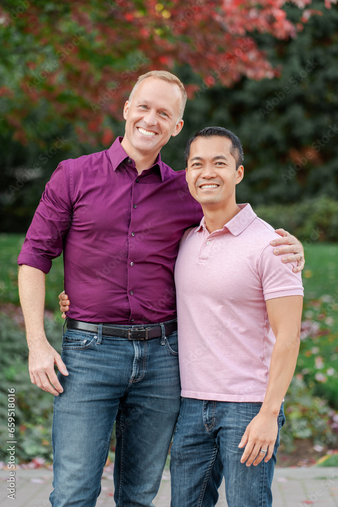 Portrait attractive smiling gay couple, two men hugging, looking at camera, posing standing in park Portrait attractive smiling gay couple, two men hugging, looking at camera, posing standing in park