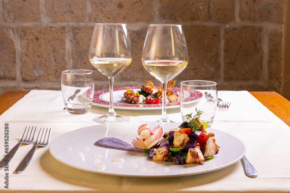 Insalata di polpo con patate viola e pomodori servita come antipasto in un ristorante elegante con un calice di vino bianco