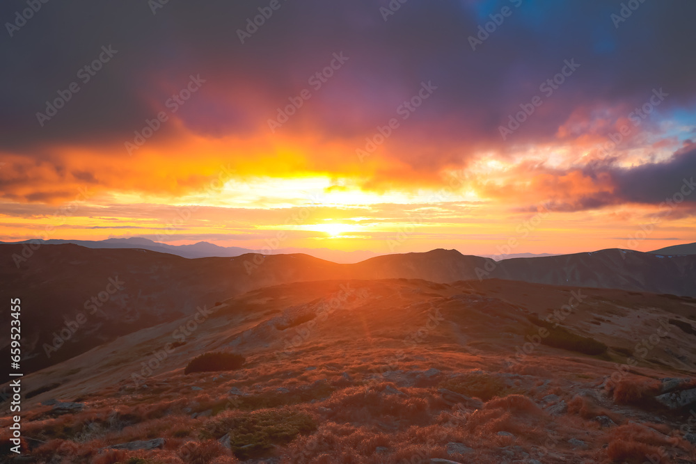 Bright orange sunset on Carpathian mountain top hill. Colorful clouds sky and highland range in background. Autumn scene. Beautiful nature summer landscape. Travel, tourism, holiday, trekking, hiking