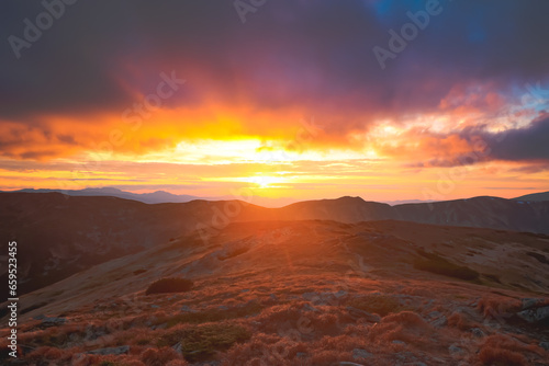 Bright orange sunset on Carpathian mountain top hill. Colorful clouds sky and highland range in background. Autumn scene. Beautiful nature summer landscape. Travel, tourism, holiday, trekking, hiking