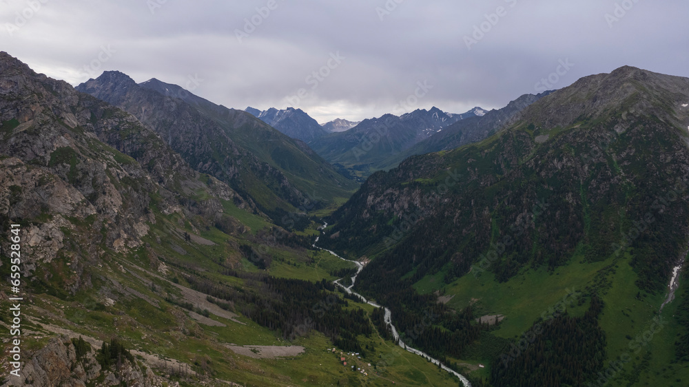 Drone view of a green gorge with high rocky cliffs. A grey, bubbling river is running. The sky was overcast. Lots of big rocks and coniferous trees. Wildlife of Kazakhstan. Gorges of Burkhan Bulak Drone view of a green gorge with high rocky cliffs. A grey, bubbling river is running. The sky was overcast. Lots of big rocks and coniferous trees. Wildlife of Kazakhstan. Gorges of Burkhan Bulak