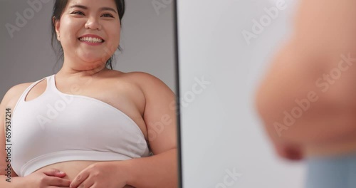A chubby Asian woman feels confident and proud of her body while standing in front of the mirror. photo