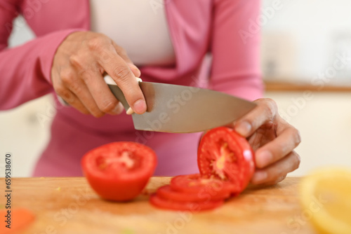 Woman cutting tomato with knife, preparing healthy breakfast in kitchen. Healthy food concept