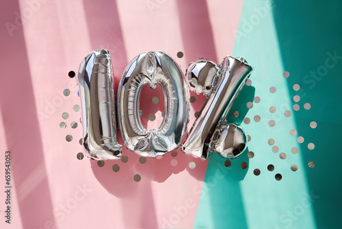 Silver numbers 10 ten percent balloons among confetti in sunlight on pink turquoise background celebration party. Greetings and congratulation