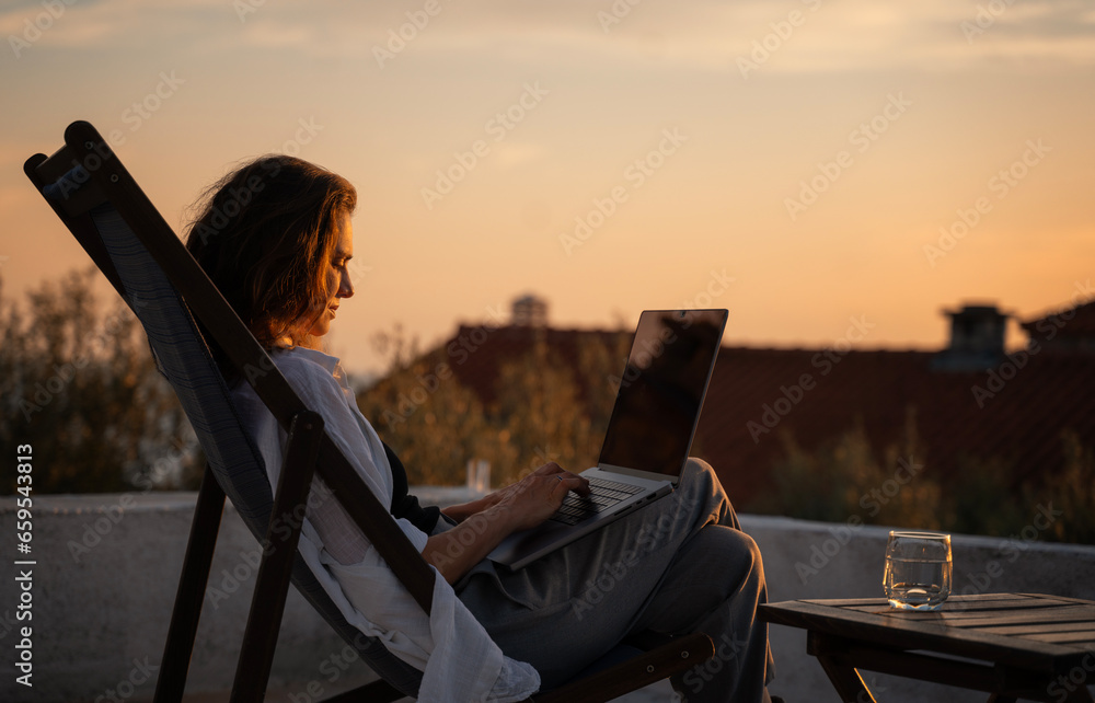 Young woman works on laptop on terrace above old town and sea