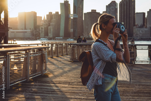 Young female tourist with rucksack taking pictures of evening city