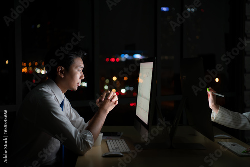 Young Asian broker international stock traders working at night in office using computer and thinking.