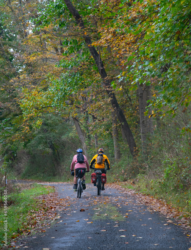 Two touring bicyclists riding together along an Autumn rural road Two touring bicyclists riding together along an Autumn rural road