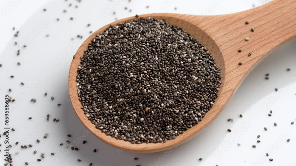 Healthy raw chia seeds in a wooden spoon on white ceramic dish close up. Rotation Healthy raw chia seeds in a wooden spoon on white ceramic dish close up. Rotation