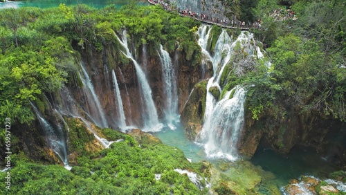 Long queue of people hiking on narrow path in Plitvice Lakes National Park Croatia. Mountain landscape with streams of water and waterfalls.