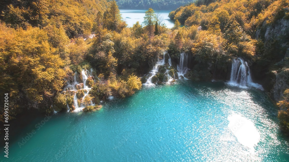 Yellow foliage on trees in autumn mountain forest with lake. Clear water of waterfalls. Emerald green reservoir. Sunny weather and bright day.