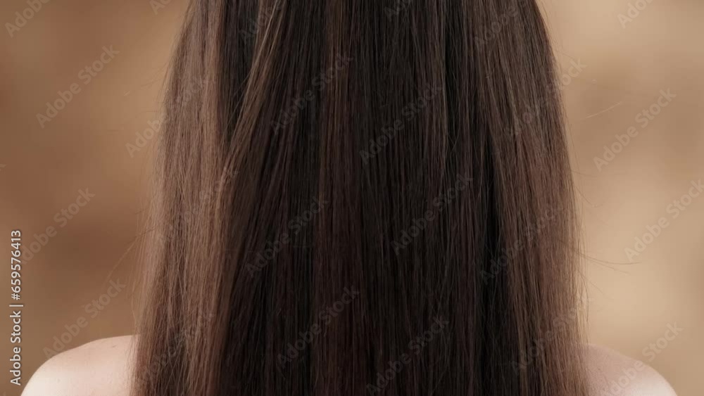 A close-up shot of a middle-aged woman against a blotchy background. She stands with her back to the camera showing off her beautiful dark, long hair. They are straight, shiny and healthy.