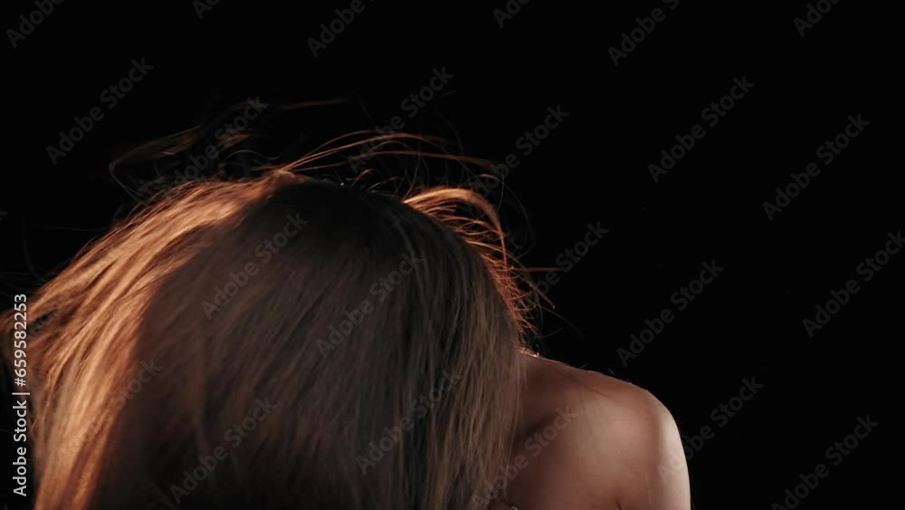 On a black background is a middle aged woman with dark hair. She is looking at the camera, waving her head and swishing her hair. The wind blows on her and develops her hair.