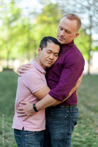 Attractive homosexual family, gay couple hugging with closed eyes standing in park on urban street © Maria Vitkovska