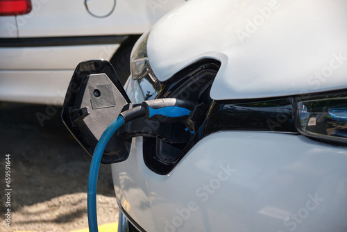 Close-up of a white electric car charging in a street parking. © SKfoto