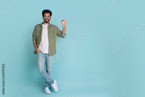 Handsome young arab man pointing at copy space on blue