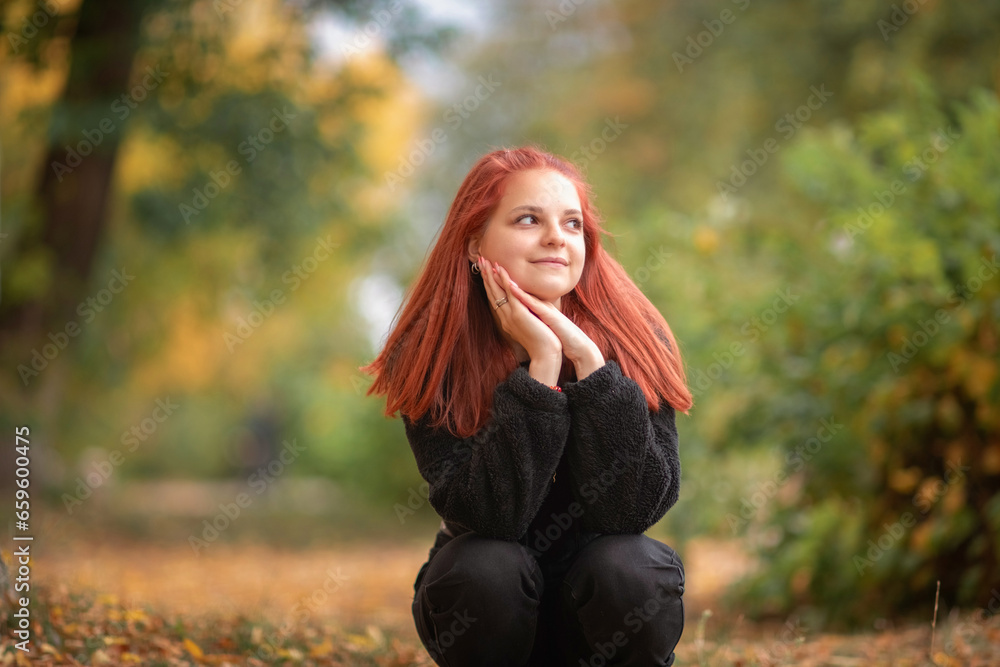 Portrait of a young beautiful red-haired girl in black jeans and a black sweater in an autumn park. Portrait of a young beautiful red-haired girl in black jeans and a black sweater in an autumn park.
