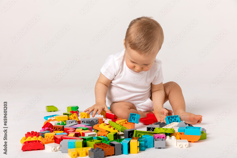 Cute baby boy in white bodysuit playing with a multicolored plastic constructor on a white background isolate, child development concept, space for text Cute baby boy in white bodysuit playing with a multicolored plastic constructor on a white background isolate, child development concept, space for text