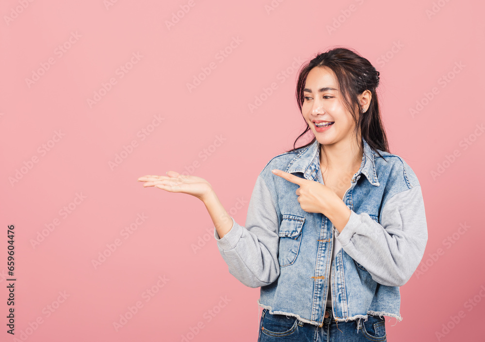 Portrait Asian beautiful young woman smiling wear denim standing pointing finger out on pink background, Thai happy face excited female point into empty looking to side away with copy space for text Portrait Asian beautiful young woman smiling wear denim standing pointing finger out on pink background, Thai happy face excited female point into empty looking to side away with copy space for text