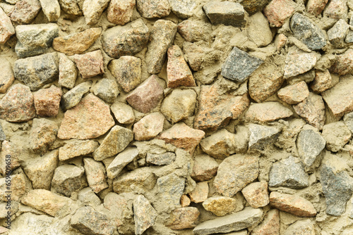 Old rough stone wall made of various square natural stones in beige, gray and brown colors.