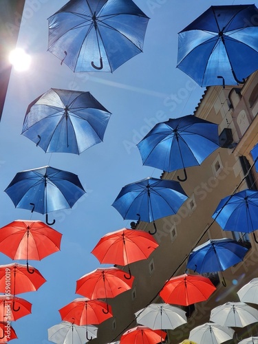 A street festively decorated with umbrellas in the colors of the tricolor suspended above the heads of pedestrians.