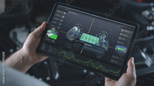 Male automotive engineer holds digital tablet computer with simulation of real-time car diagnostics or developing displayed on screen. 3D render of program with 3D virtual electric vehicle prototype. photo