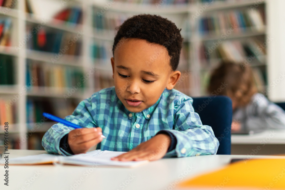 Focused schoolboy writing in copybook during lesson in classroom Focused schoolboy writing in copybook during lesson in classroom