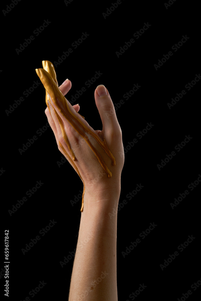 Fototapeta premium Female hand in liquid gold on a black background.