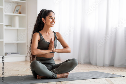 Happy millennial eastern lady practicing yoga at home
